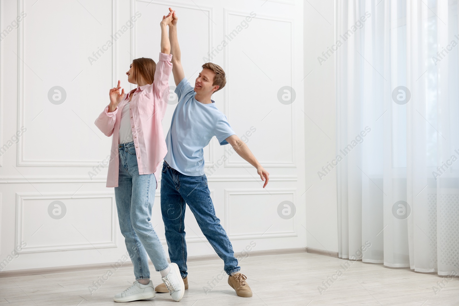 Happy couple dancing together near white wall at home Photo of Happy couple dancing together near white wall at home