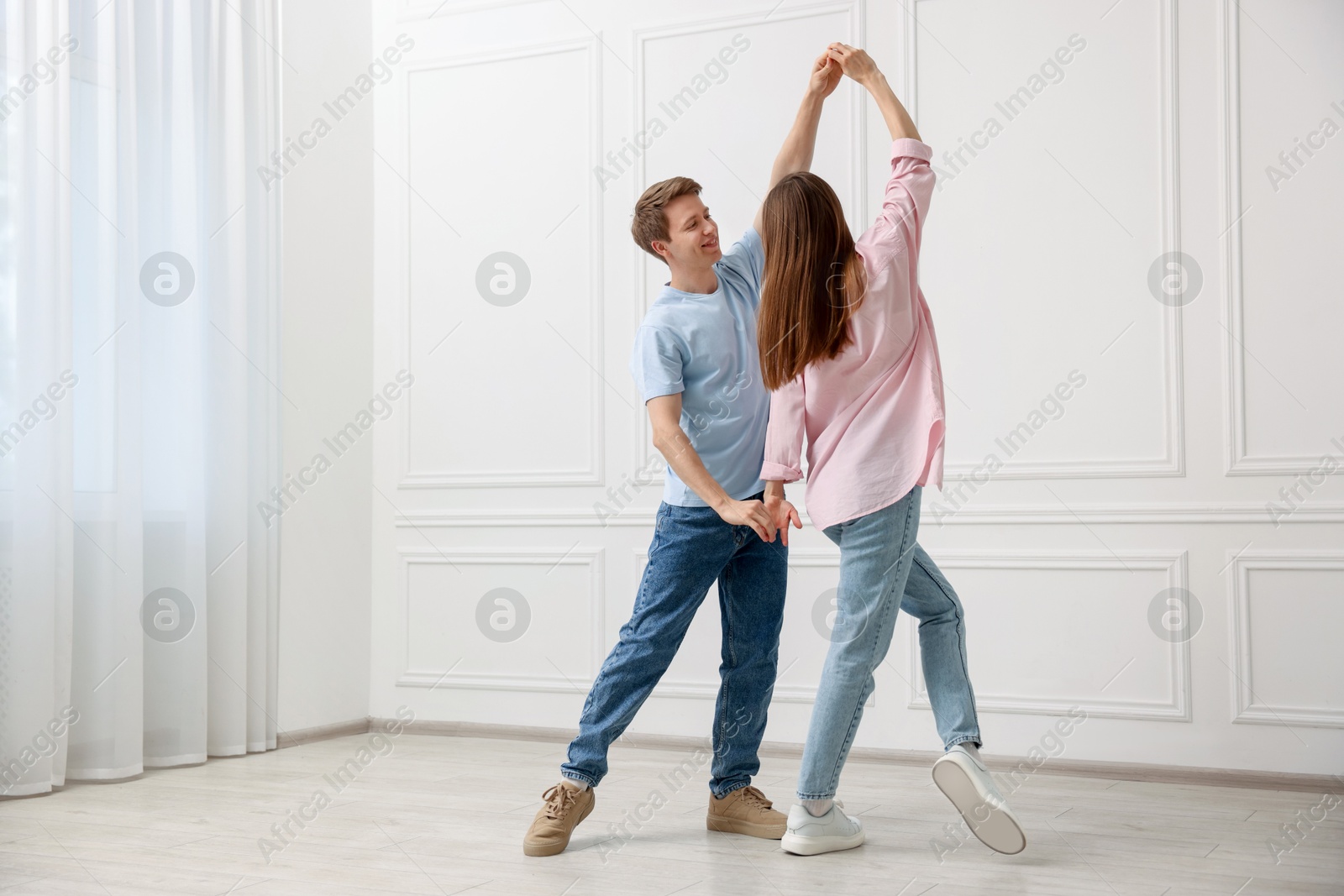 Happy couple dancing together near white wall at home Photo of Happy couple dancing together near white wall at home