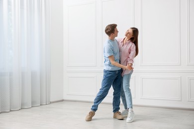 Photo of Happy couple dancing together near white wall at home. Space for text
