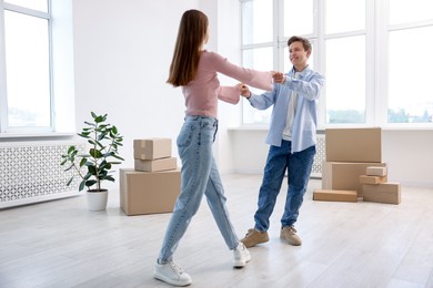 Photo of Happy young couple dancing and cardboard boxes at home, low angle view. Moving day