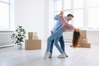 Photo of Happy young couple dancing and cardboard boxes at home, low angle view. Moving day