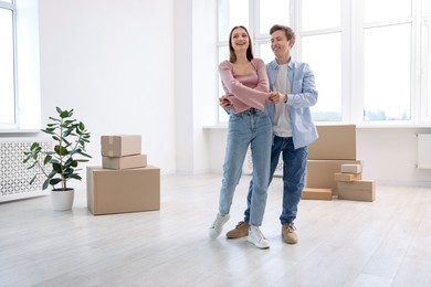 Photo of Happy young couple dancing and cardboard boxes at home, low angle view. Moving day