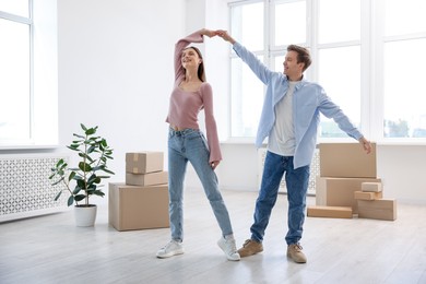 Photo of Happy young couple dancing and cardboard boxes at home. Moving day