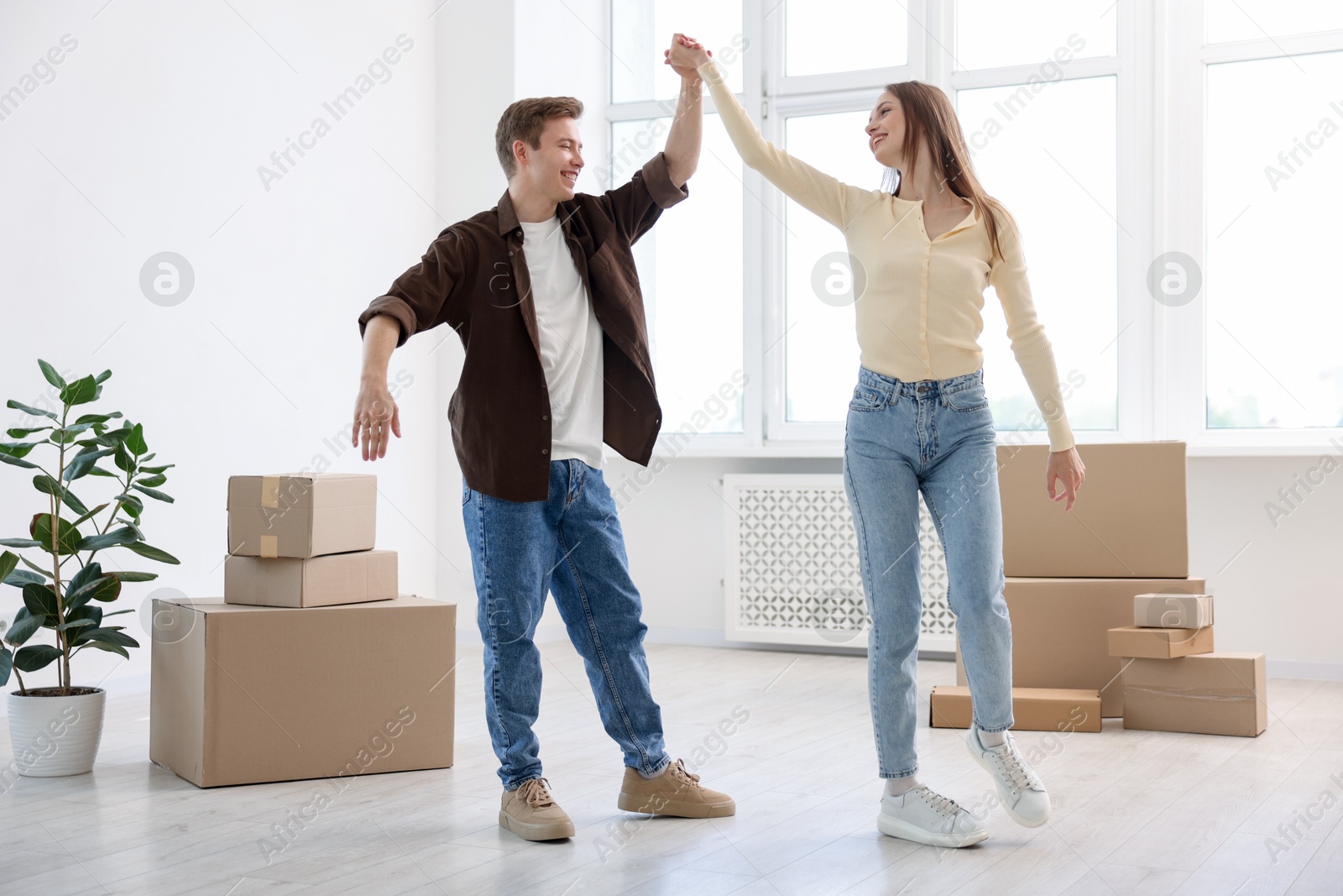 Photo of Happy young couple dancing and cardboard boxes at home, low angle view. Moving day