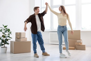 Photo of Happy young couple dancing and cardboard boxes at home, low angle view. Moving day