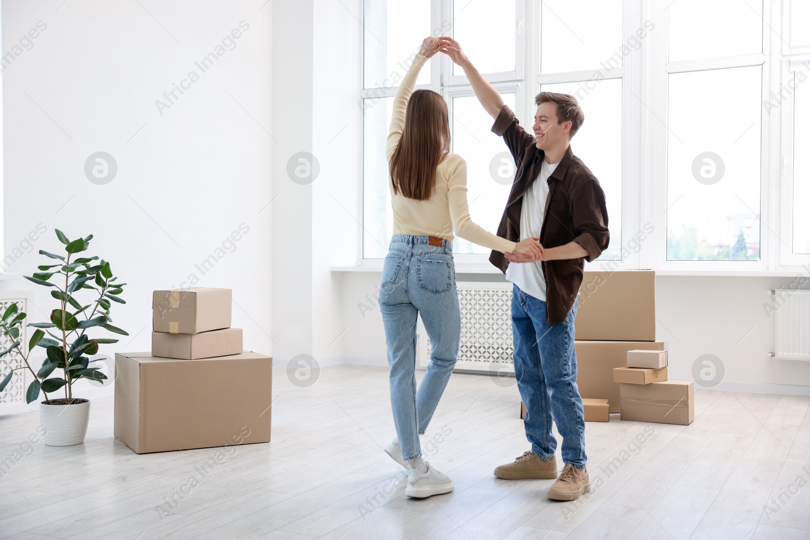 Photo of Happy young couple dancing and cardboard boxes at home. Moving day