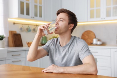 Photo of Man drinking water from glass at wooden table in kitchen