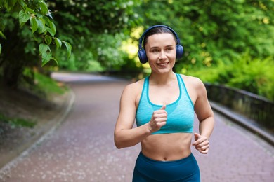 Photo of Sporty woman with headphones running in park, space for text