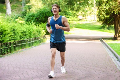 Photo of Sporty man with headphones running in park