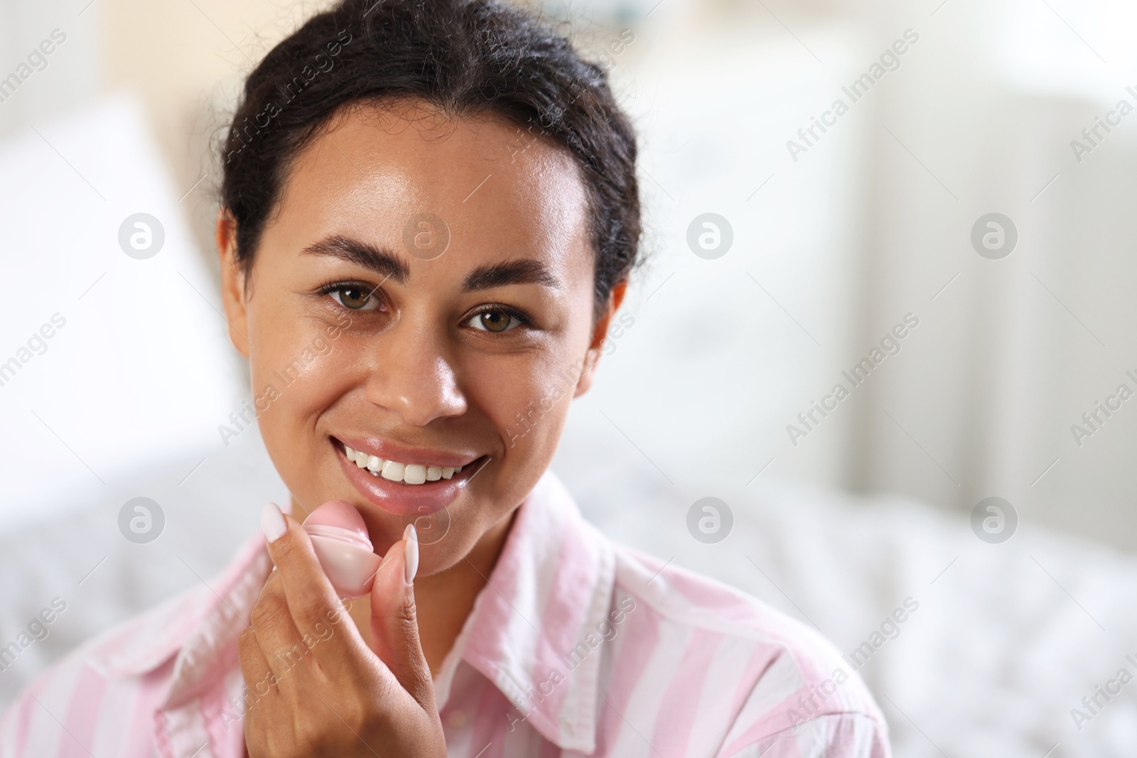 Smiling woman with lip balm on blurred background. Space for text Photo of Smiling woman with lip balm on blurred background. Space for text