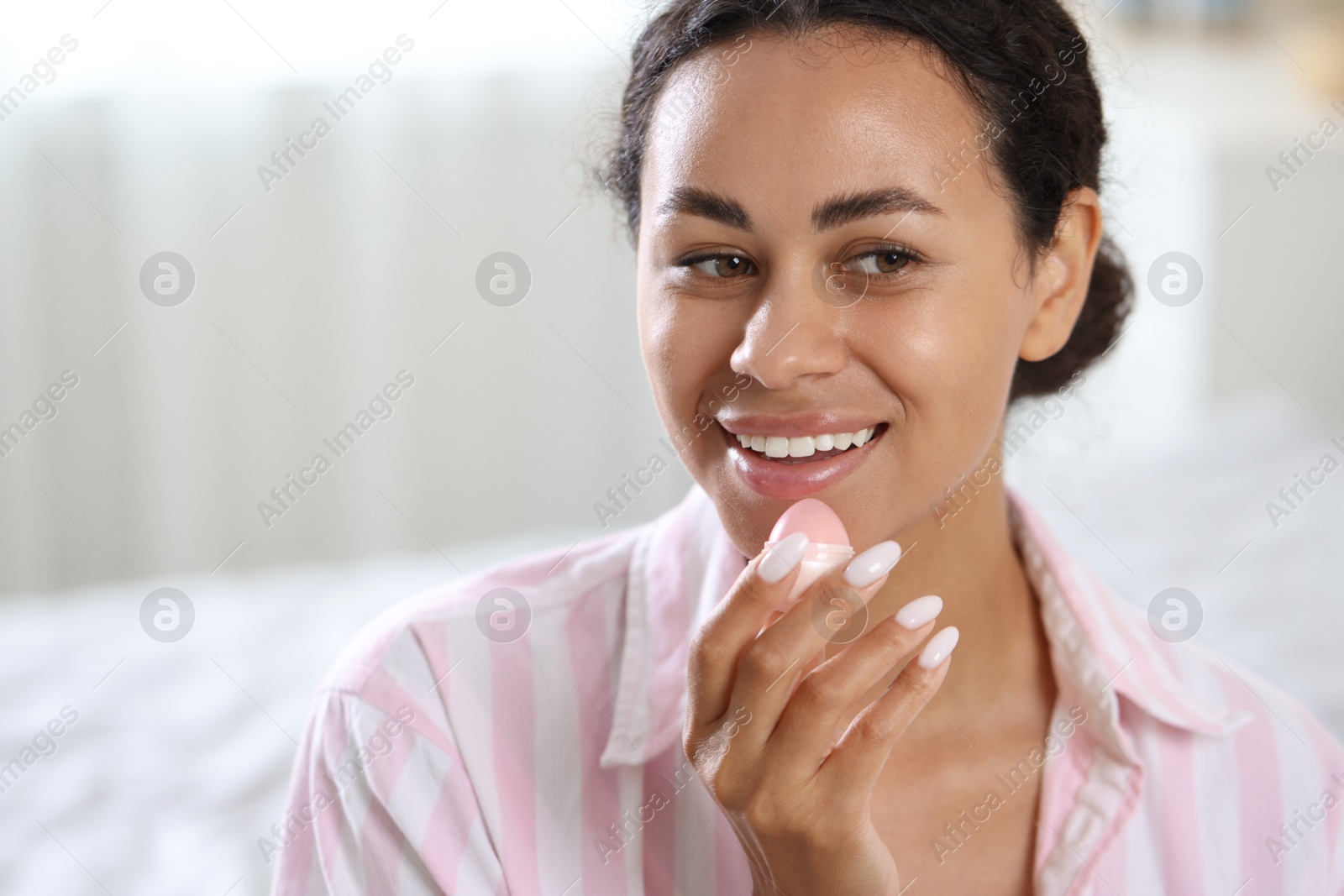 Photo of Smiling woman with lip balm on blurred background. Space for text