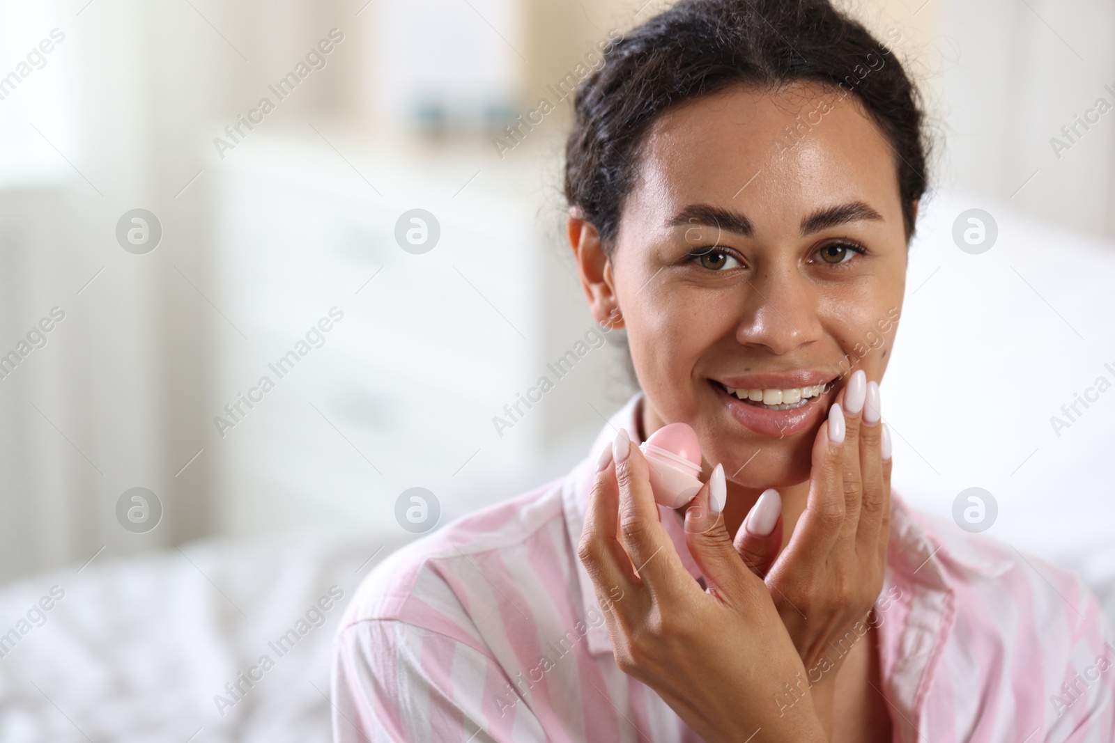 Photo of Smiling woman with lip balm on blurred background. Space for text