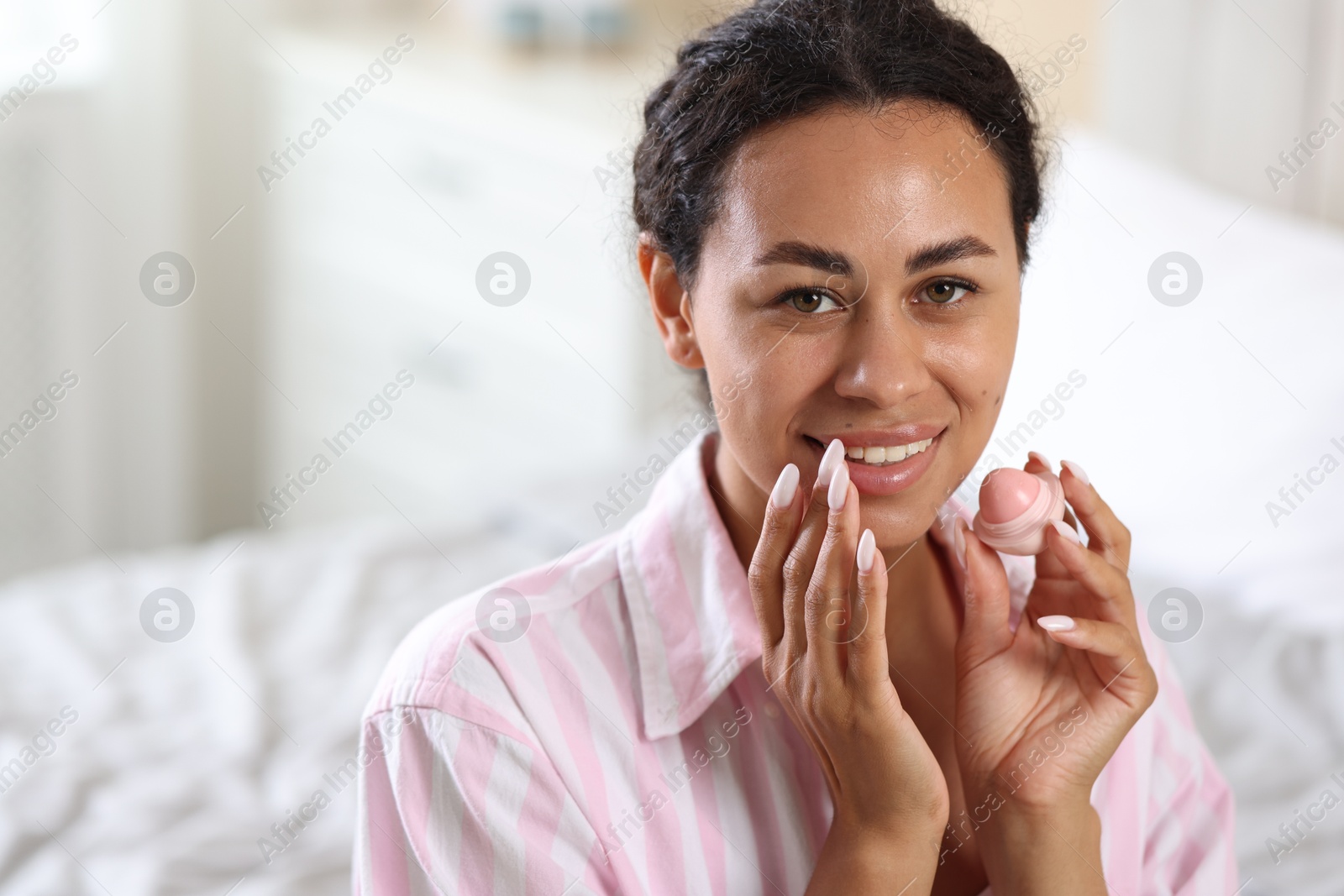 Smiling woman with lip balm on blurred background. Space for text Photo of Smiling woman with lip balm on blurred background. Space for text