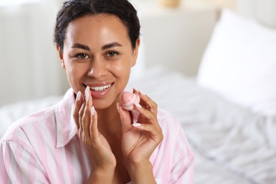 Photo of Smiling woman with lip balm on blurred background. Space for text