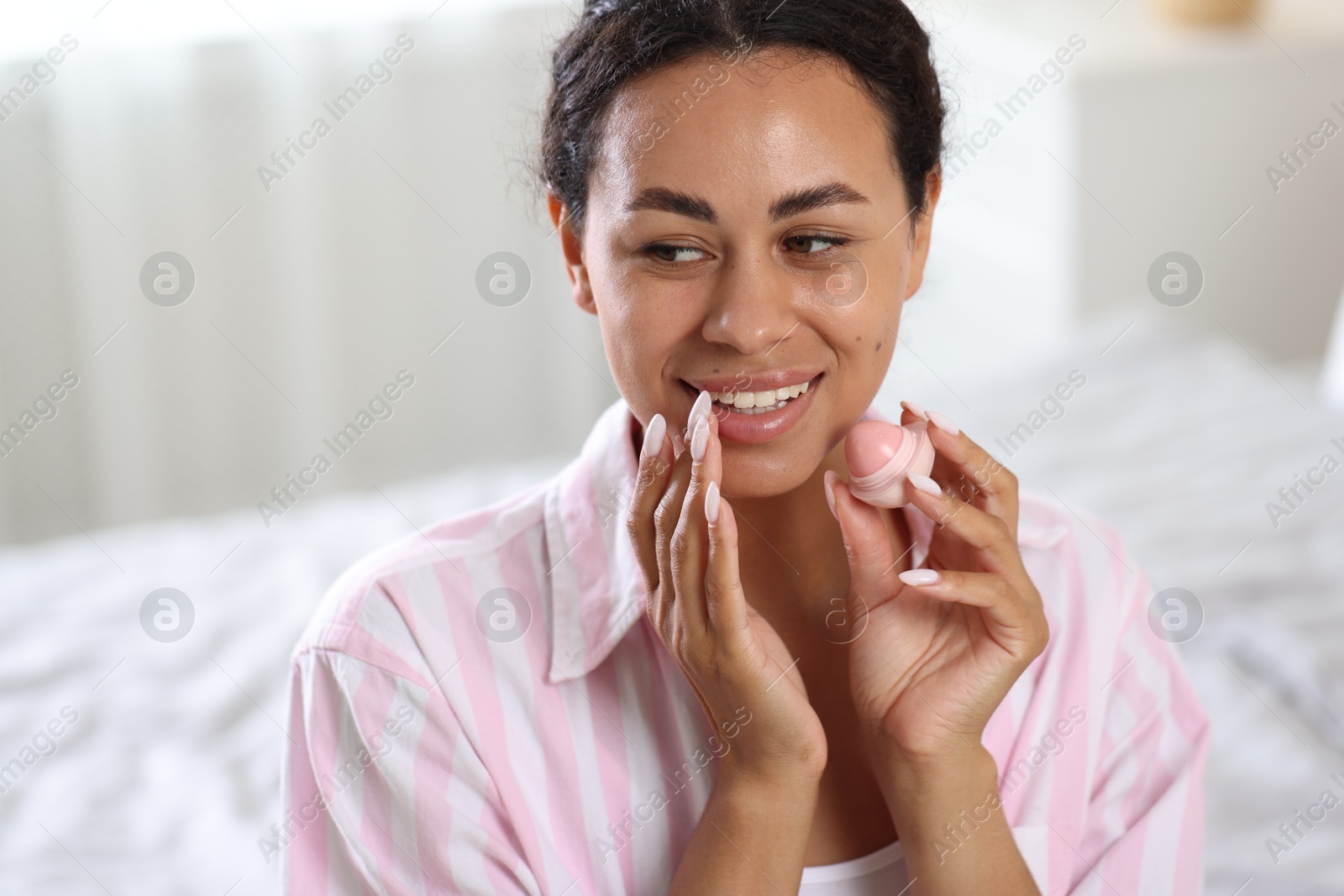 Smiling woman with lip balm on blurred background, closeup Photo of Smiling woman with lip balm on blurred background, closeup