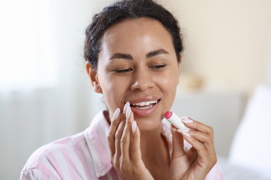 Photo of Smiling woman applying lip balm onto her lips on blurred background, closeup