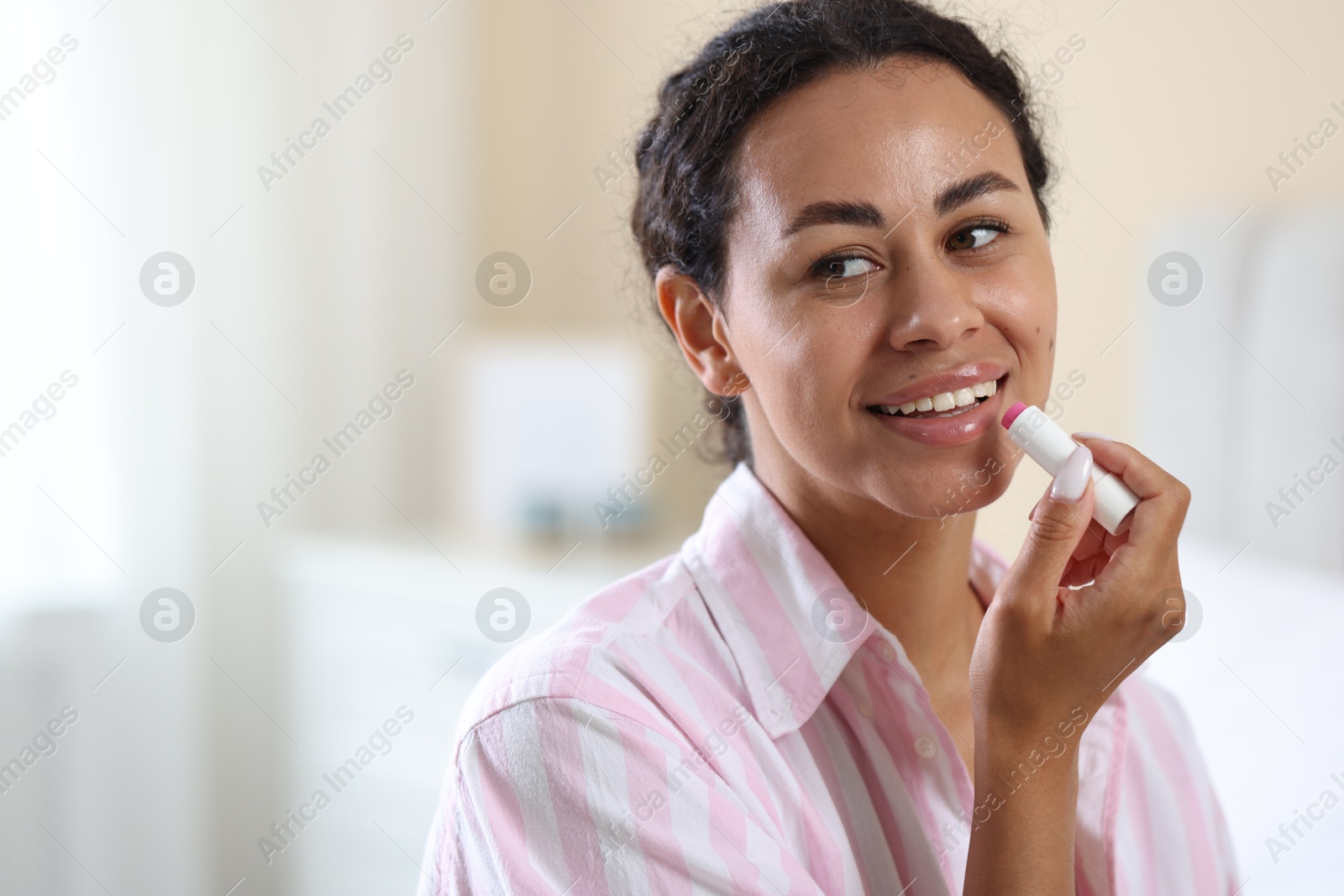 Smiling woman applying lip balm onto her lips on blurred background, closeup. Space for text Photo of Smiling woman applying lip balm onto her lips on blurred background, closeup. Space for text
