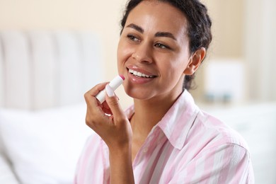 Photo of Smiling woman applying lip balm onto her lips on blurred background, closeup