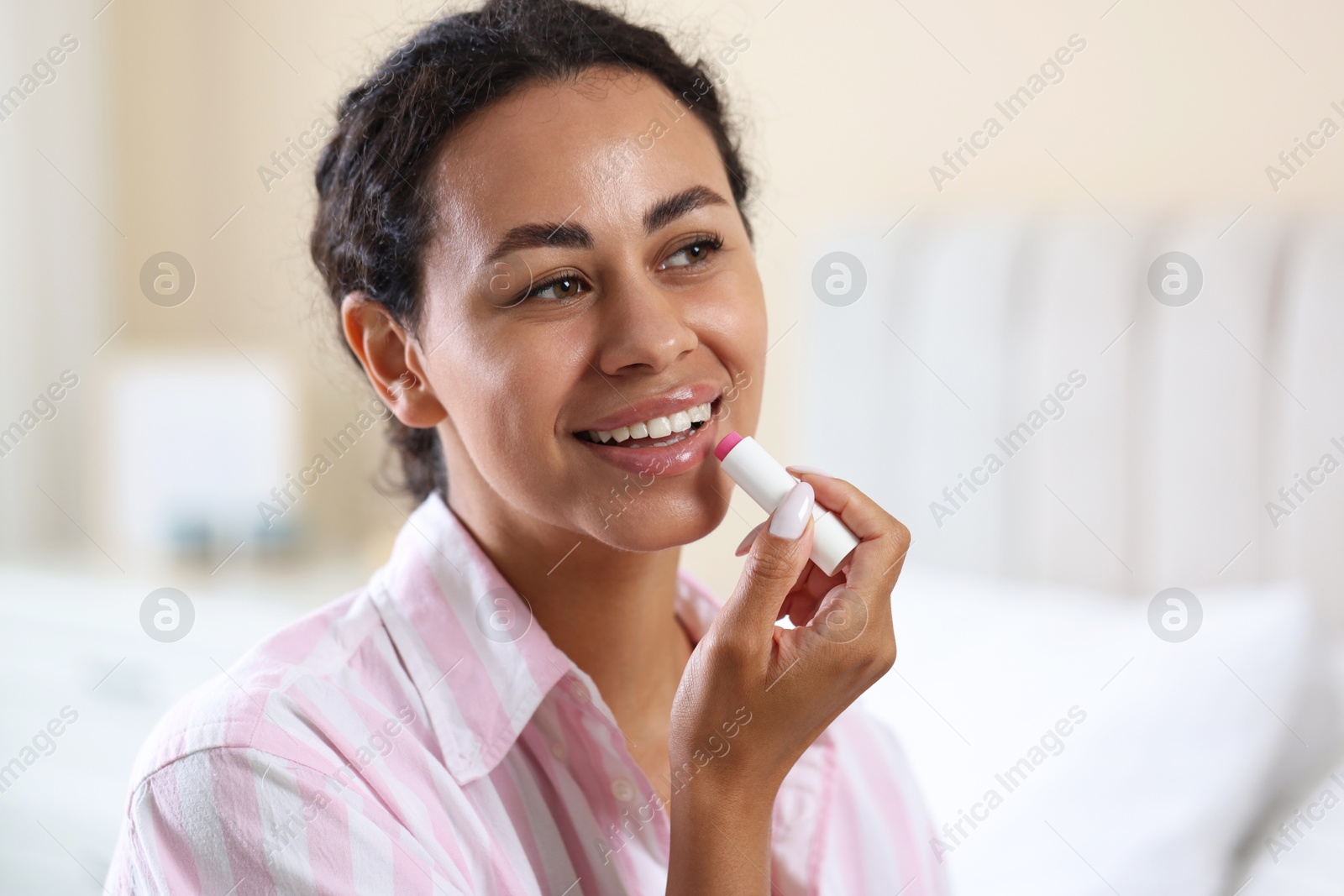 Smiling woman applying lip balm onto her lips on blurred background, closeup Photo of Smiling woman applying lip balm onto her lips on blurred background, closeup
