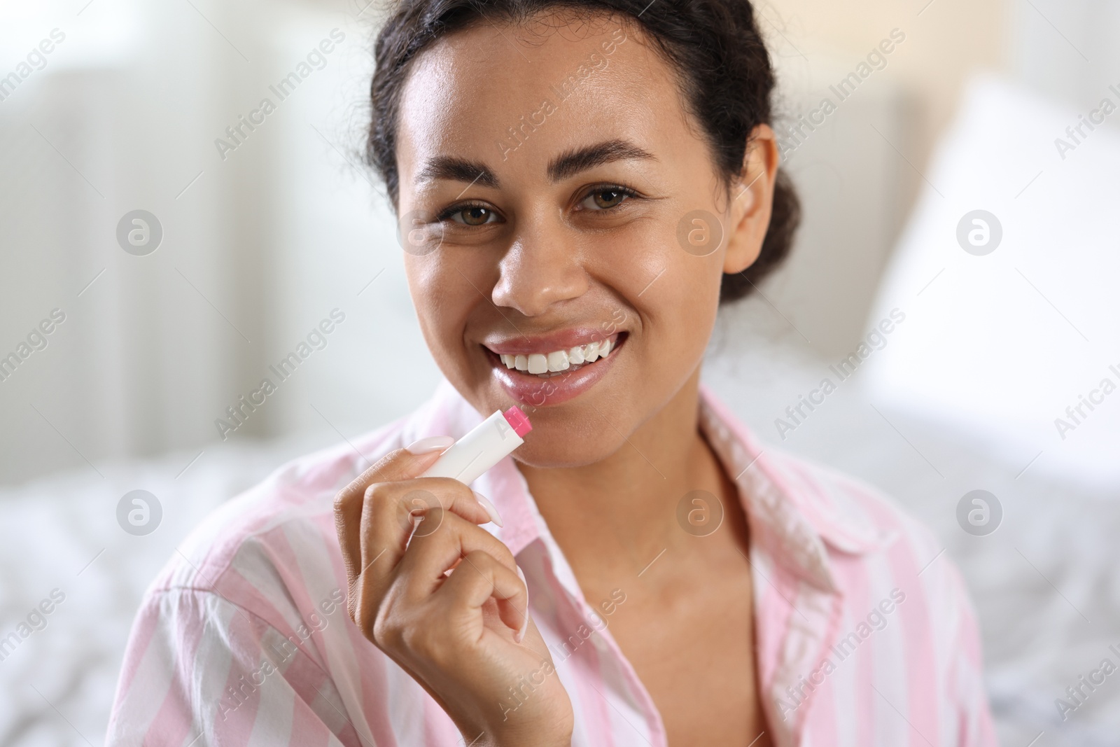Smiling woman with lip balm on blurred background, closeup Photo of Smiling woman with lip balm on blurred background, closeup