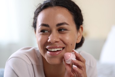 Photo of Smiling woman with lip balm on blurred background, closeup