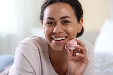 Photo of Smiling woman with lip balm on blurred background, closeup