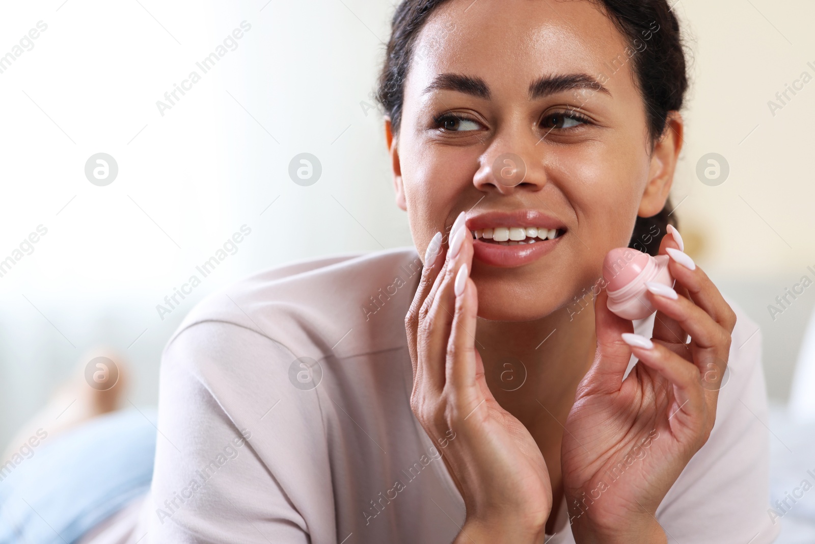 Photo of Smiling woman with lip balm on blurred background, closeup