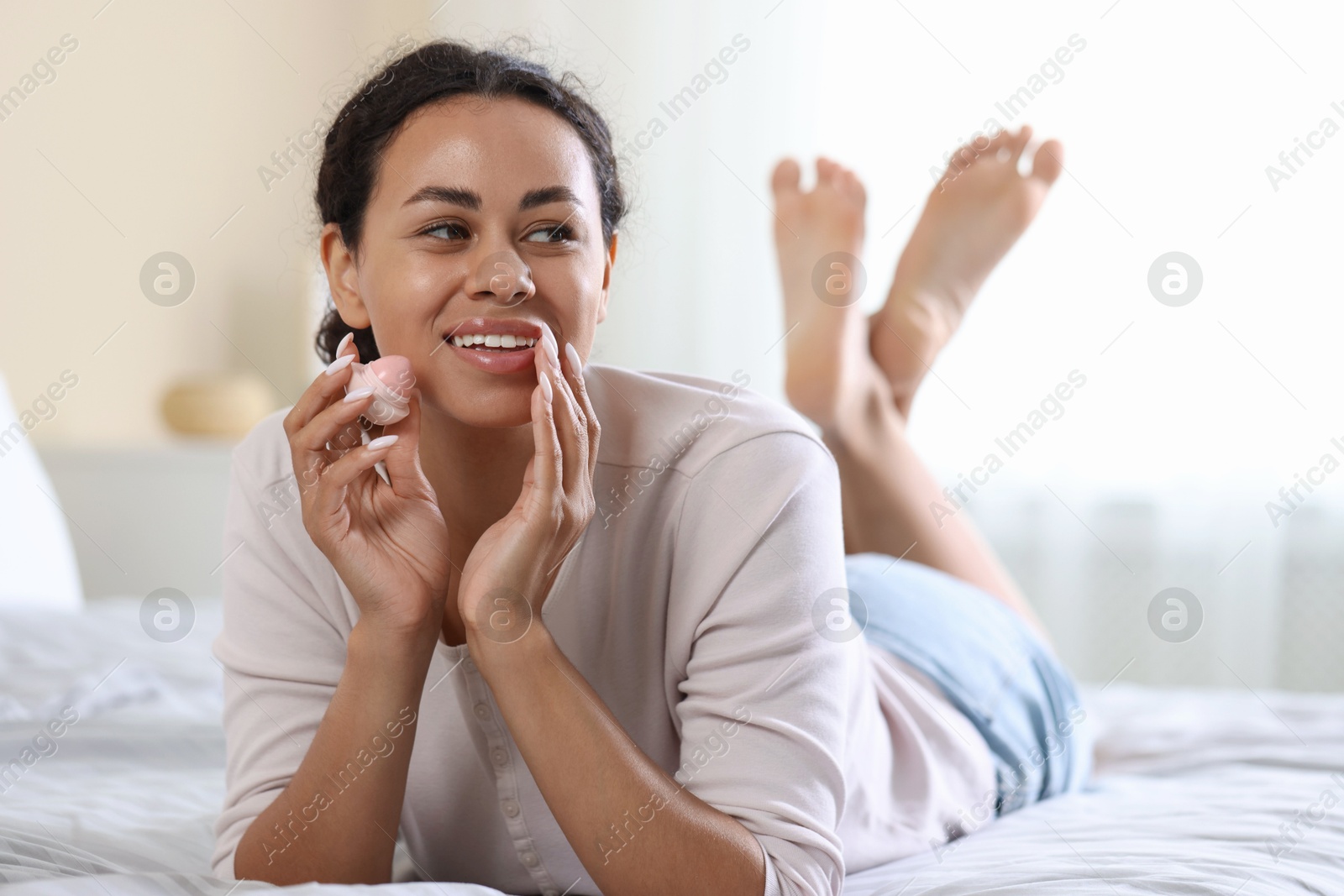Smiling woman with lip balm on bed indoors Photo of Smiling woman with lip balm on bed indoors