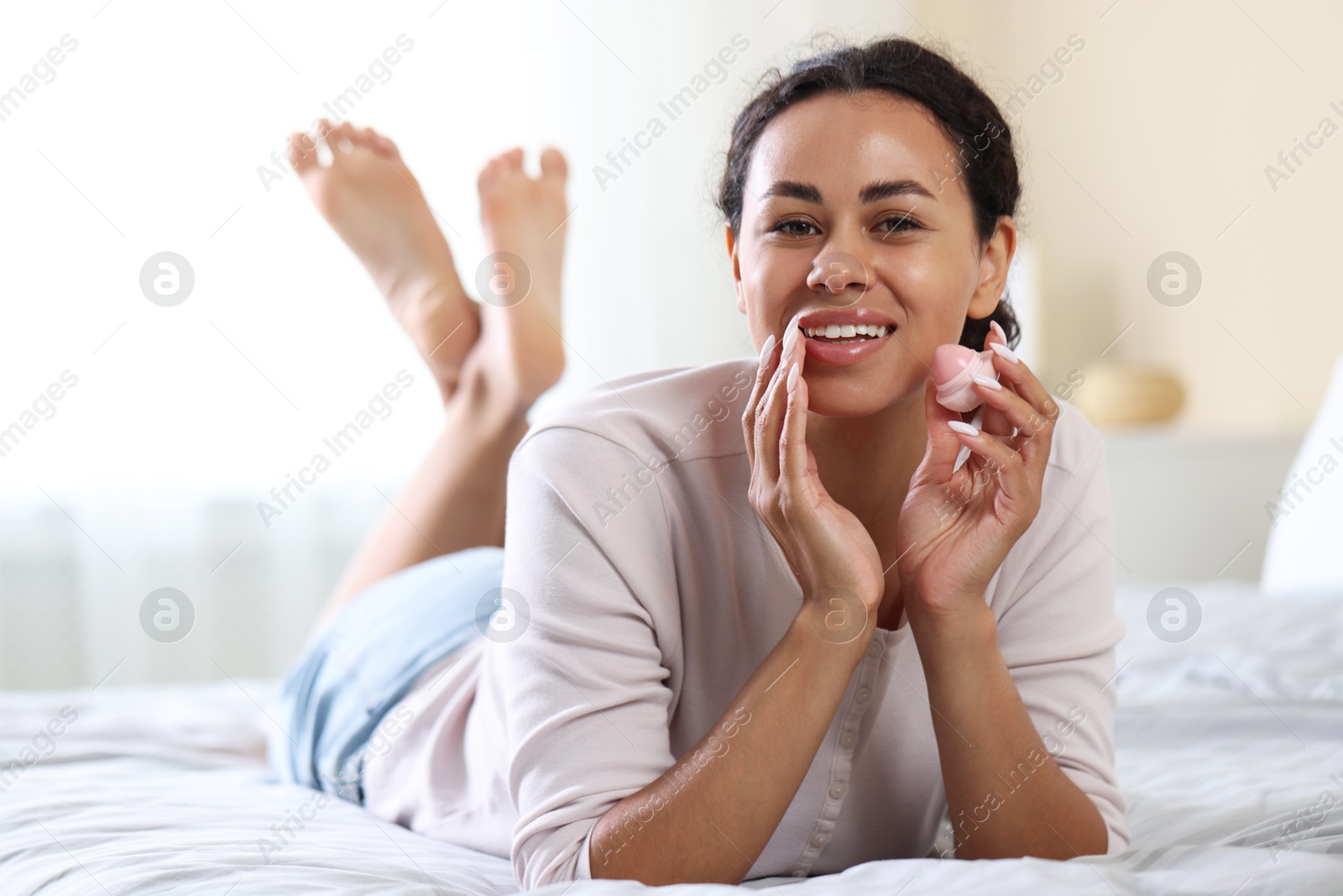 Smiling woman with lip balm on bed indoors Photo of Smiling woman with lip balm on bed indoors