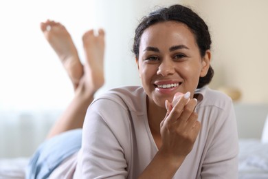 Photo of Smiling woman with lip balm on bed indoors