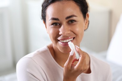 Photo of Smiling woman applying lip balm onto her lips on blurred background, closeup
