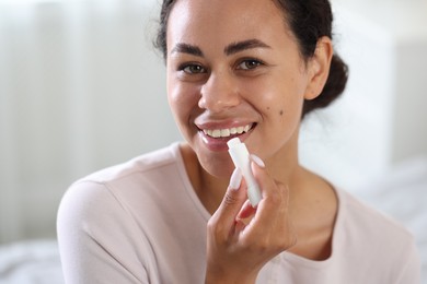 Photo of Smiling woman applying lip balm onto her lips on blurred background, closeup