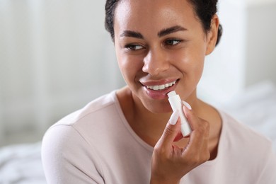 Photo of Smiling woman applying lip balm onto her lips on blurred background, closeup