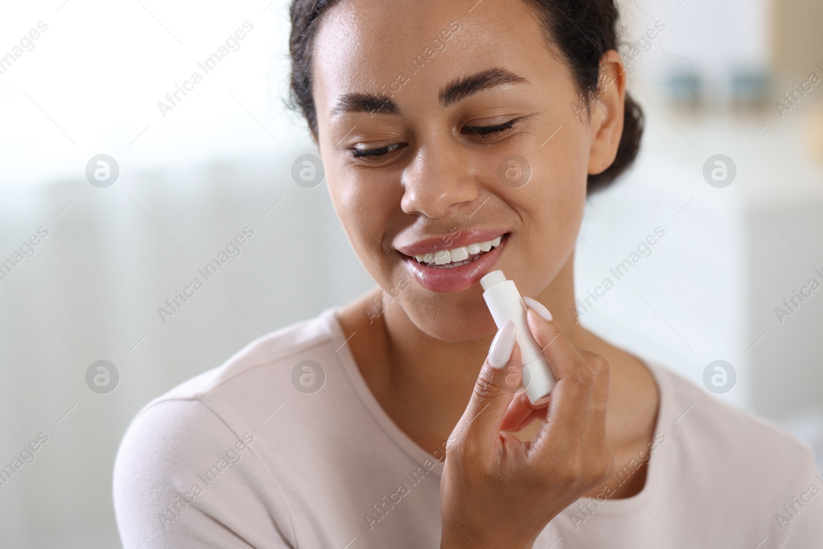 Smiling woman applying lip balm onto her lips on blurred background, closeup Photo of Smiling woman applying lip balm onto her lips on blurred background, closeup