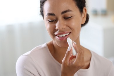 Photo of Smiling woman applying lip balm onto her lips on blurred background, closeup