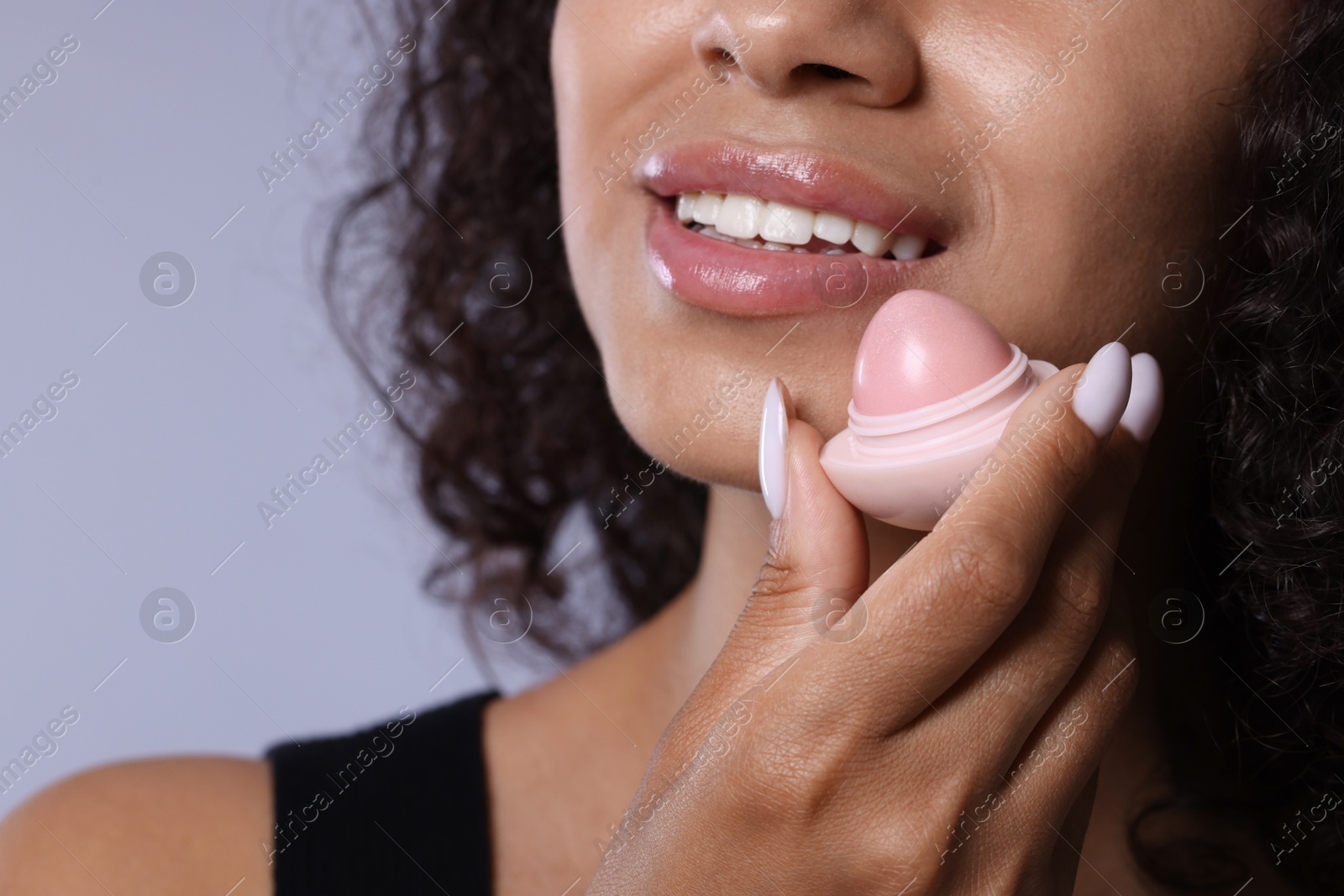 Smiling woman with lip balm on grey background, closeup Photo of Smiling woman with lip balm on grey background, closeup