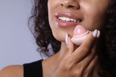 Photo of Smiling woman with lip balm on grey background, closeup