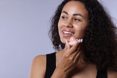 Photo of Smiling woman with lip balm on grey background, closeup
