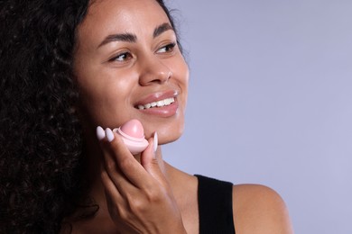 Photo of Smiling woman with lip balm on grey background, closeup