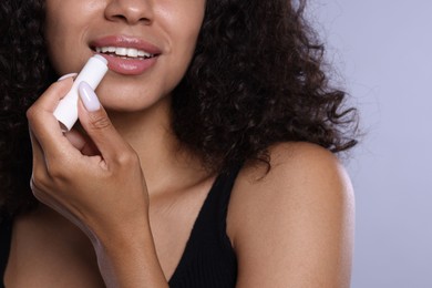 Photo of Smiling woman applying lip balm onto her lips on grey background, closeup