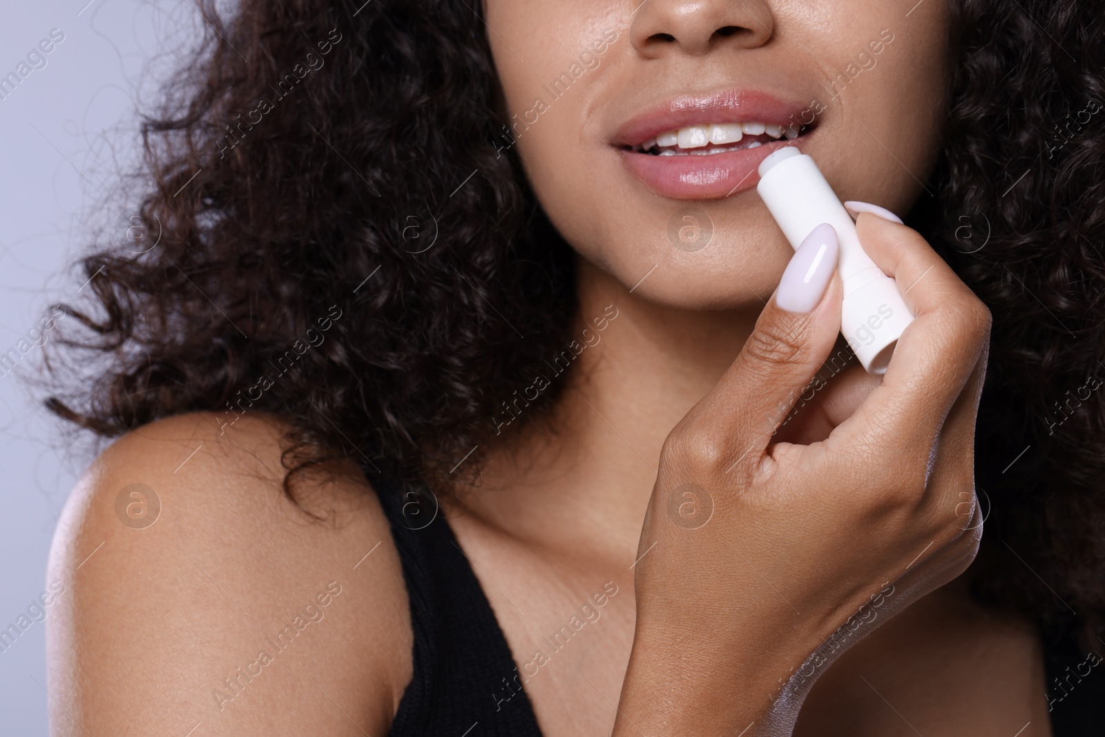 Smiling woman applying lip balm onto her lips on grey background, closeup Photo of Smiling woman applying lip balm onto her lips on grey background, closeup