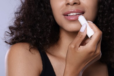 Photo of Smiling woman applying lip balm onto her lips on grey background, closeup