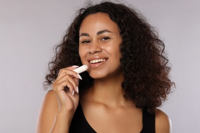 Photo of Smiling woman applying lip balm onto her lips on grey background