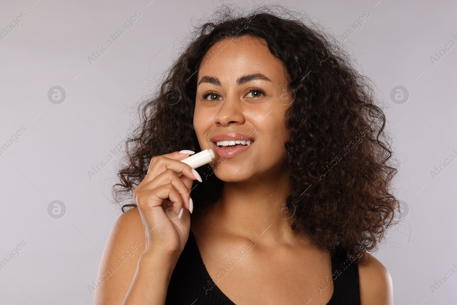 Smiling woman applying lip balm onto her lips on grey background Photo of Smiling woman applying lip balm onto her lips on grey background
