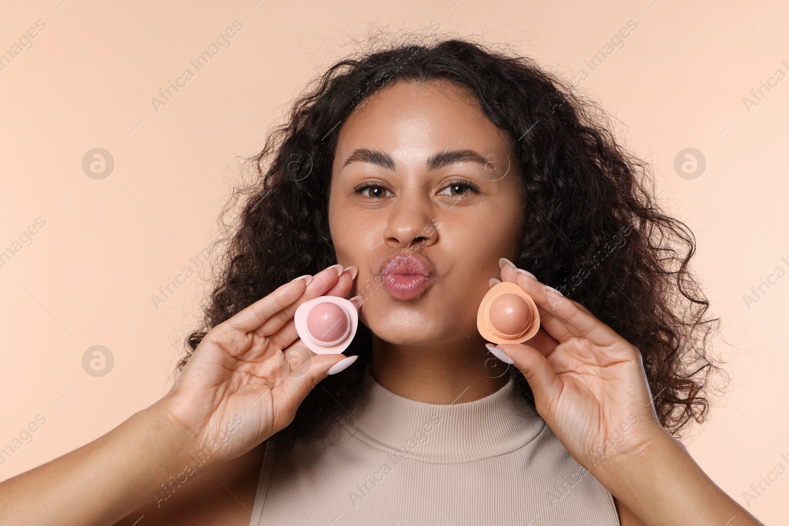 Beautiful woman with containers of lip balm on beige background Photo of Beautiful woman with containers of lip balm on beige background