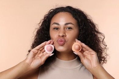 Photo of Beautiful woman with containers of lip balm on beige background