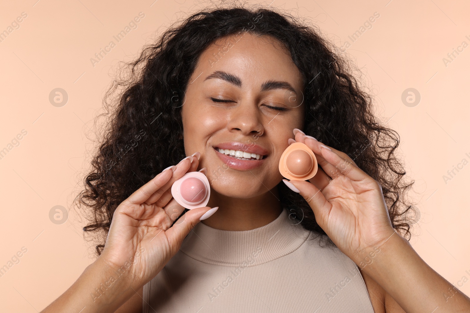 Smiling woman with containers of lip balm on beige background Photo of Smiling woman with containers of lip balm on beige background