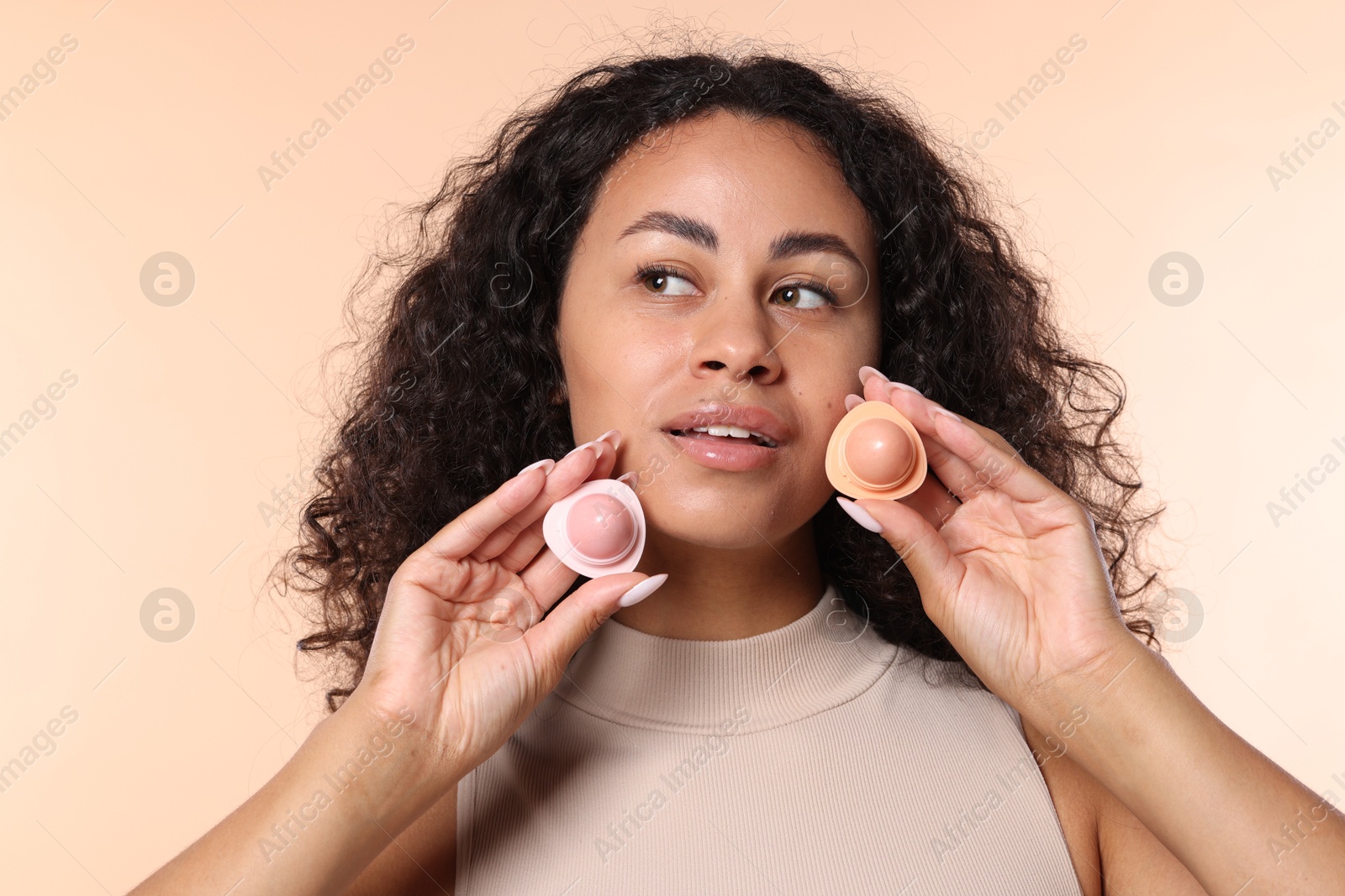 Photo of Smiling woman with containers of lip balm on beige background