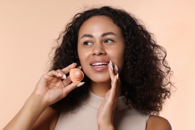Photo of Smiling woman with lip balm on beige background, closeup