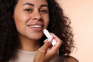 Photo of Smiling woman applying lip balm onto her lips on beige background, closeup